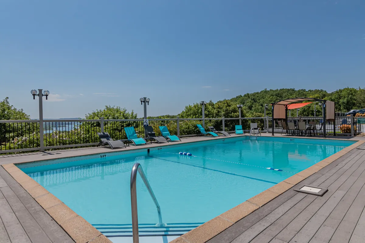 This image features a sparkling outdoor swimming pool surrounded by lounge chairs, a canopy area for shade, and lush natural greenery in the background. The space looks inviting for both relaxation and social gatherings, with the pool as the central focus.