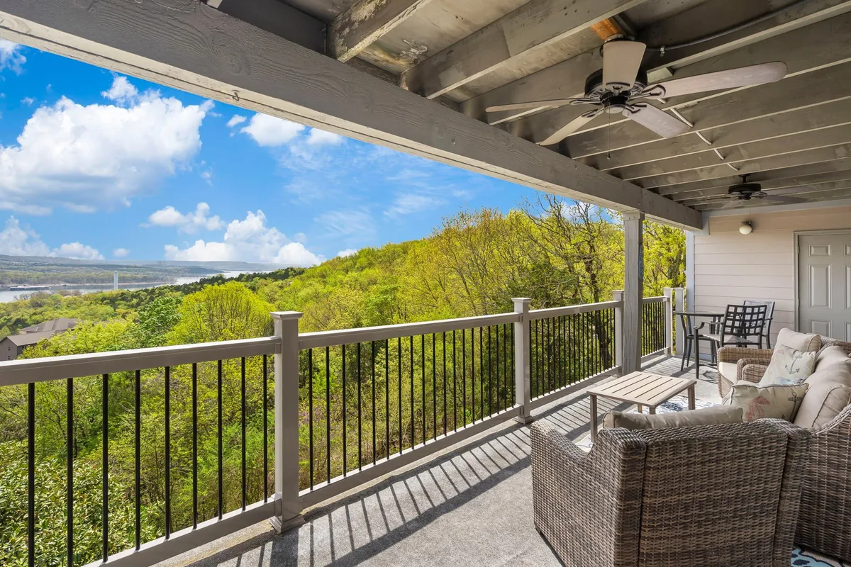 A spacious balcony with inviting cushioned seating arranged to maximize enjoyment of the panoramic lake view. The deck overlooks Table Rock Lake, with greenery visible in the distance, and the outdoor furniture is ideal for both relaxation and dining. The setting is serene, suggesting sunrise coffee or starlit evenings.