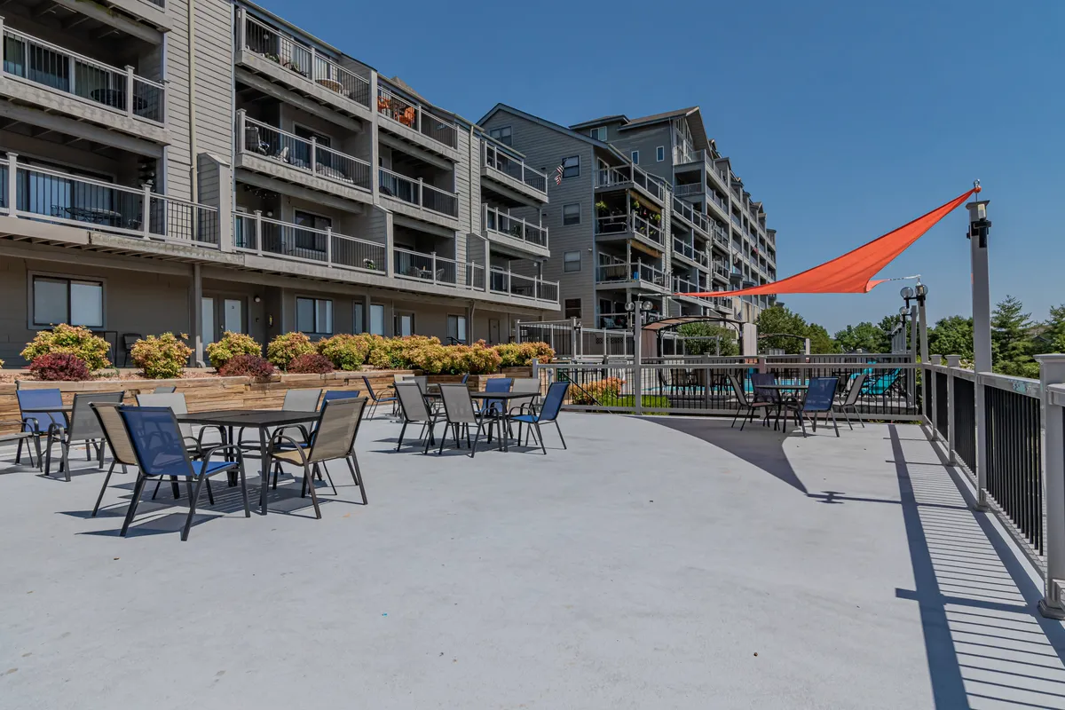 This image captures a welcoming outdoor seating area adorned with a colorful awning, surrounded by flower beds and neighboring buildings. There’s a sense of community, relaxation, and enjoyment under the sun, with ample space for guests to gather, dine, or simply unwind.