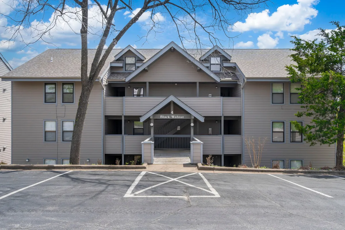 The welcoming entrance of the property, marked by a 'Black Walnut' sign, multiple levels, and large windows. The scene captures an inviting space for afternoon picnics or evening gatherings under the stars, setting the tone for arrival and social connection.