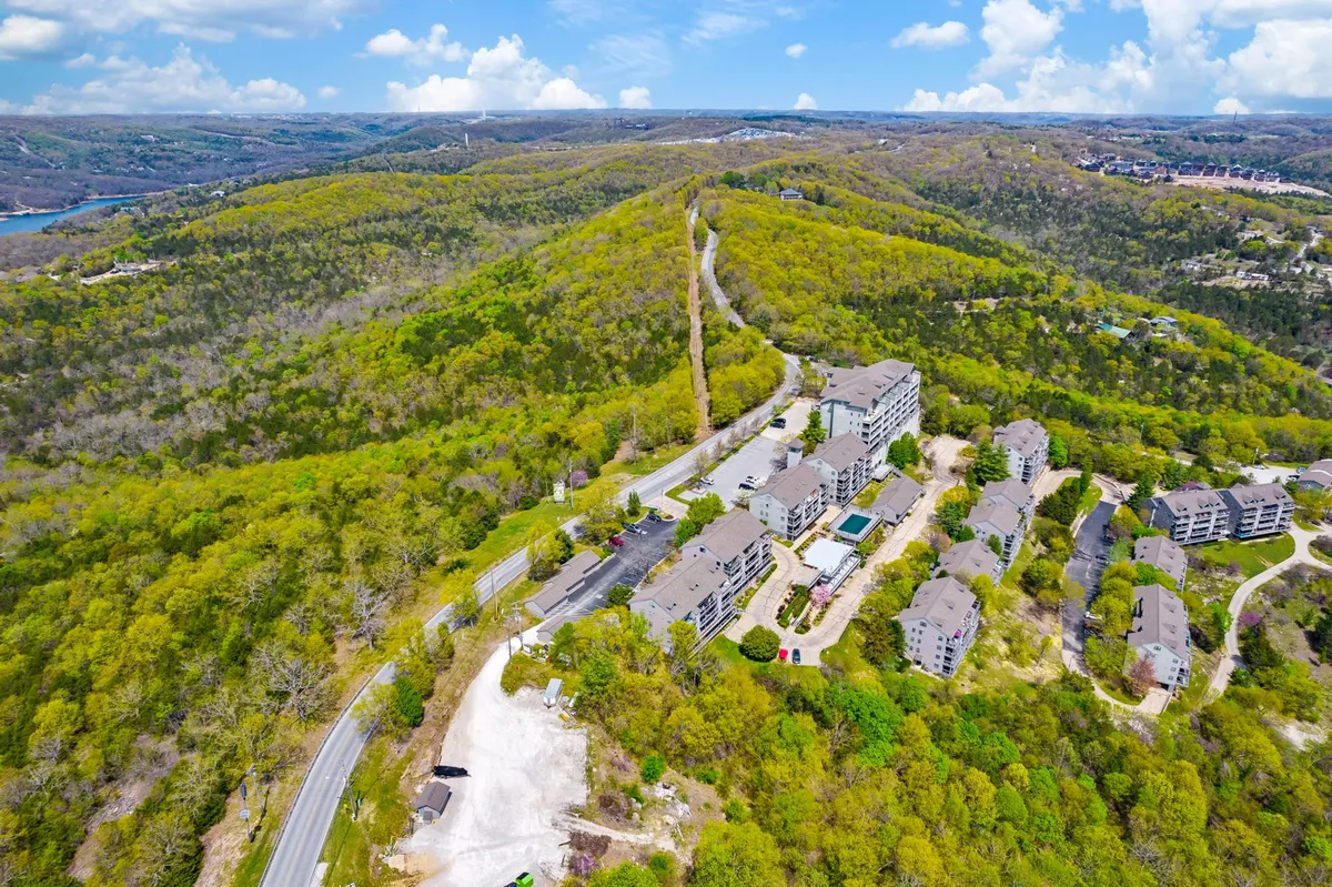 A wide view of rolling green hills, a cluster of buildings, and an outdoor swimming pool area, set in a tranquil natural environment. The perspective emphasizes both spaciousness and community, ideal for group activities or evening strolls.