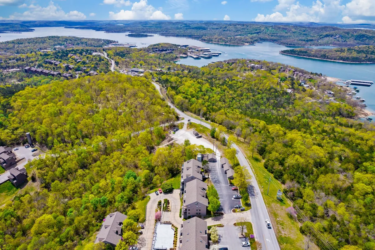 This scenic view captures lush green trees and clear blue water, dotted with residential buildings and a winding road. The setting invites outdoor exploration, boating, swimming, and nature walks, all activities highlighted in the section.