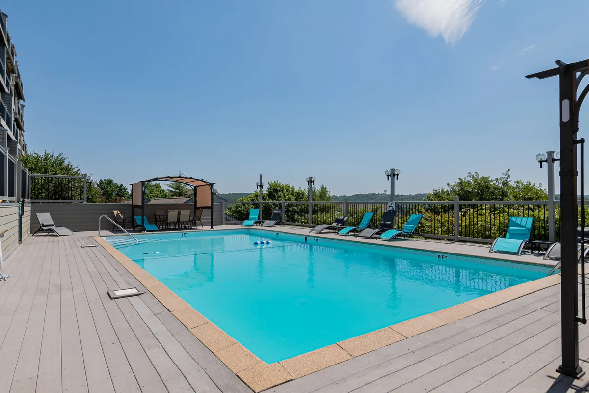 A vibrant outdoor swimming pool area with loungers, a cabana, and landscaped surroundings, set against a scenic backdrop. The image radiates a cheerful, relaxed mood, suggesting a place for socializing, pool parties, or unwinding after a day of golf or boating.