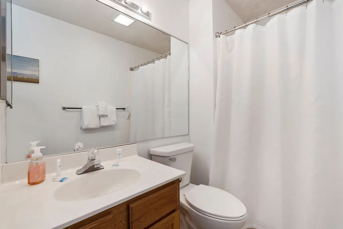 A bright, fresh bathroom featuring a sink, mirror, and shower curtain. The space is clean and inviting, ideal for morning routines or unwinding with a soothing shower after a day of activity.
